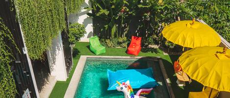 A swimming pool with a unicorn float, surrounded by greenery and yellow umbrellas.