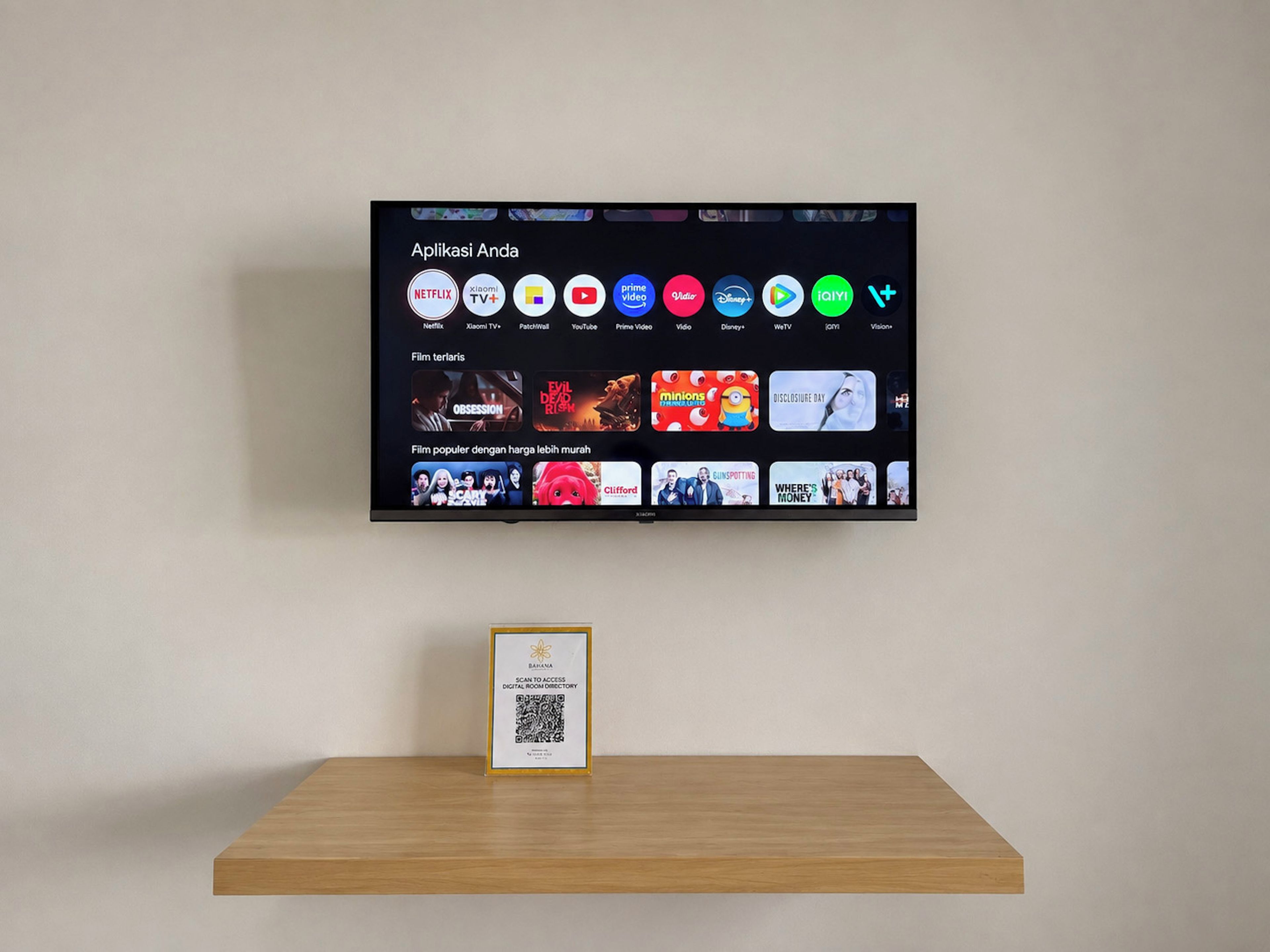 A flat-screen TV mounted on a wall displaying a streaming service interface with various apps and movie thumbnails.