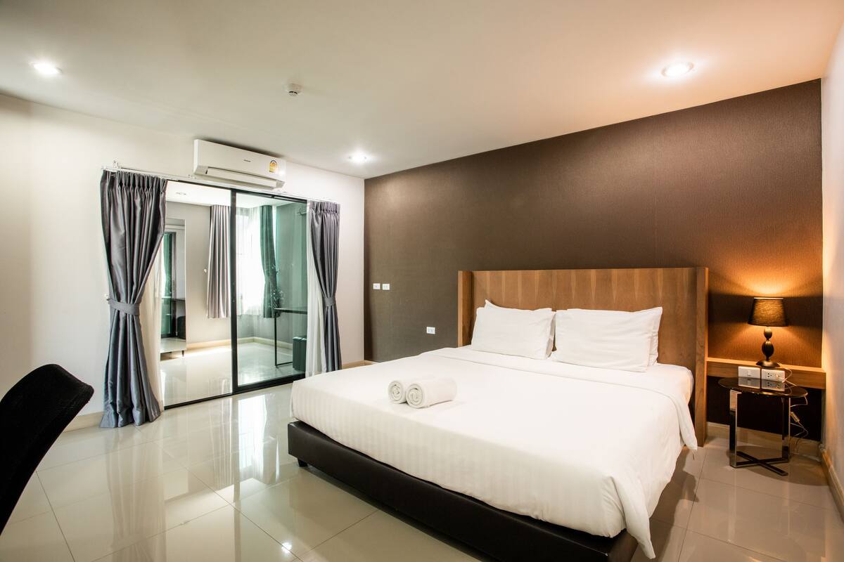 Een moderne hotelkamer met een groot bed, een douchegedeelte van glas en een klein nachtkastje met een lamp.