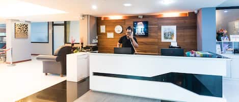 A modern reception desk with a digital screen, a clock, and a wooden panel wall.