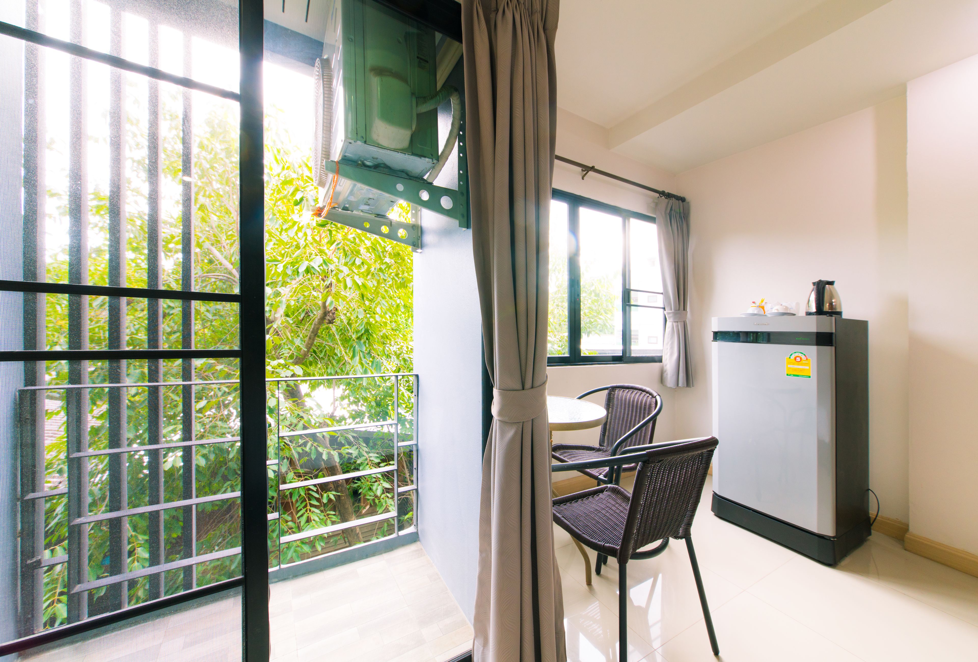 A room with a balcony, a table with chairs, a refrigerator, and a window with curtains.
