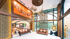 A spacious lobby with a high ceiling, a wine rack, and a large window offering a view of the outdoors. - Jira Boutique Residence (Chiang Mai)