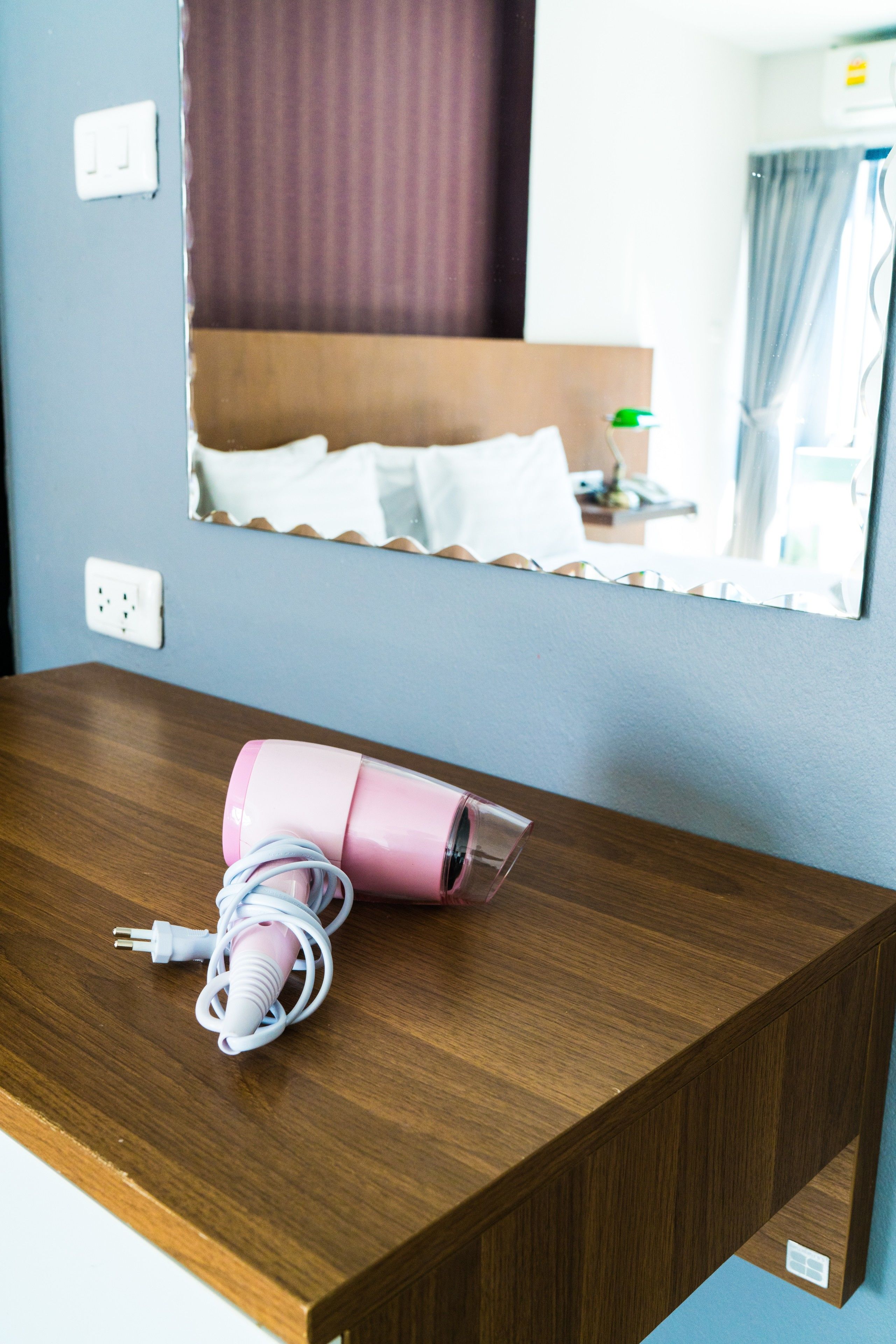 A wooden bedside table with a pink hairdryer and its charging cable.