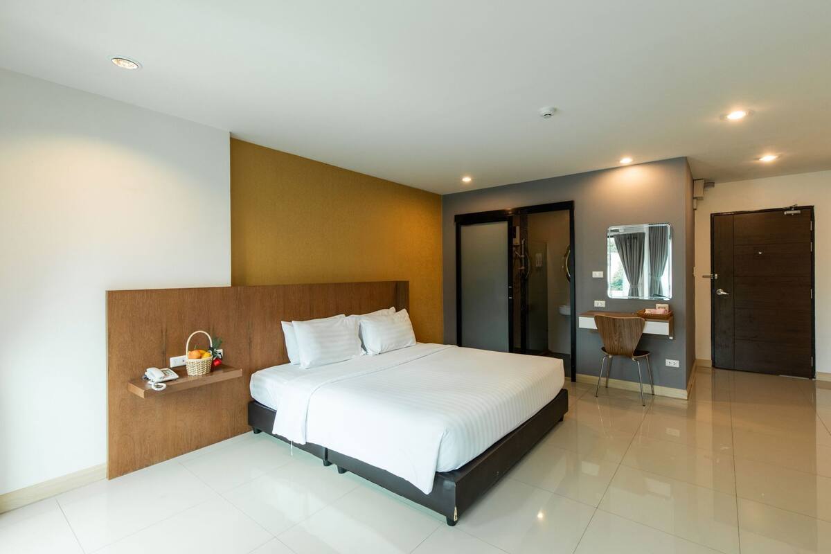 Een moderne hotelkamer met een groot bed, een nachtkastje met telefoon en mandje, een bureau met stoel en een donkere deur.