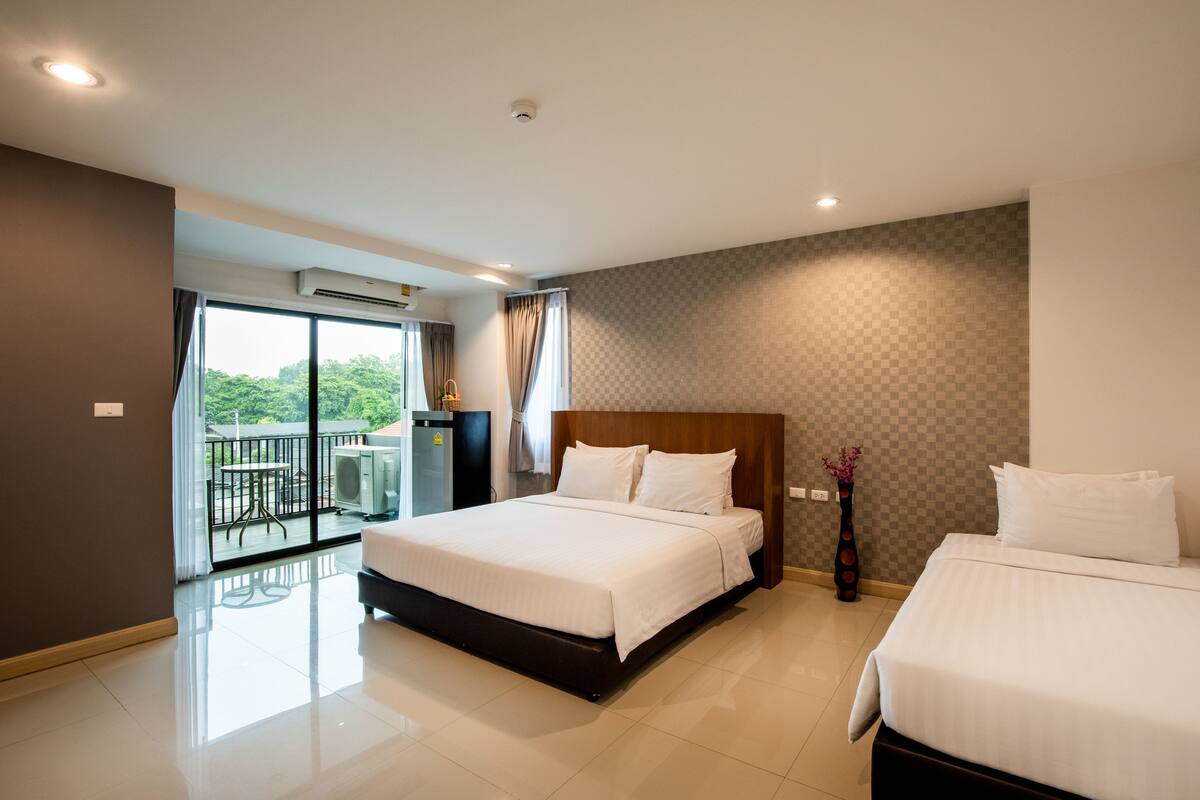 Een hotelkamer met een groot bed, een kleiner bed, een balkon met een tafel en stoelen, en een airconditioning.
