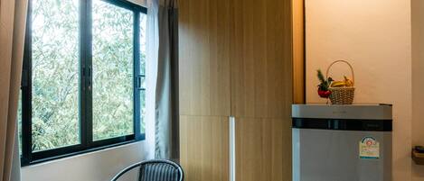A compact room with a window, a table with a chair, a refrigerator, and a wooden wardrobe.