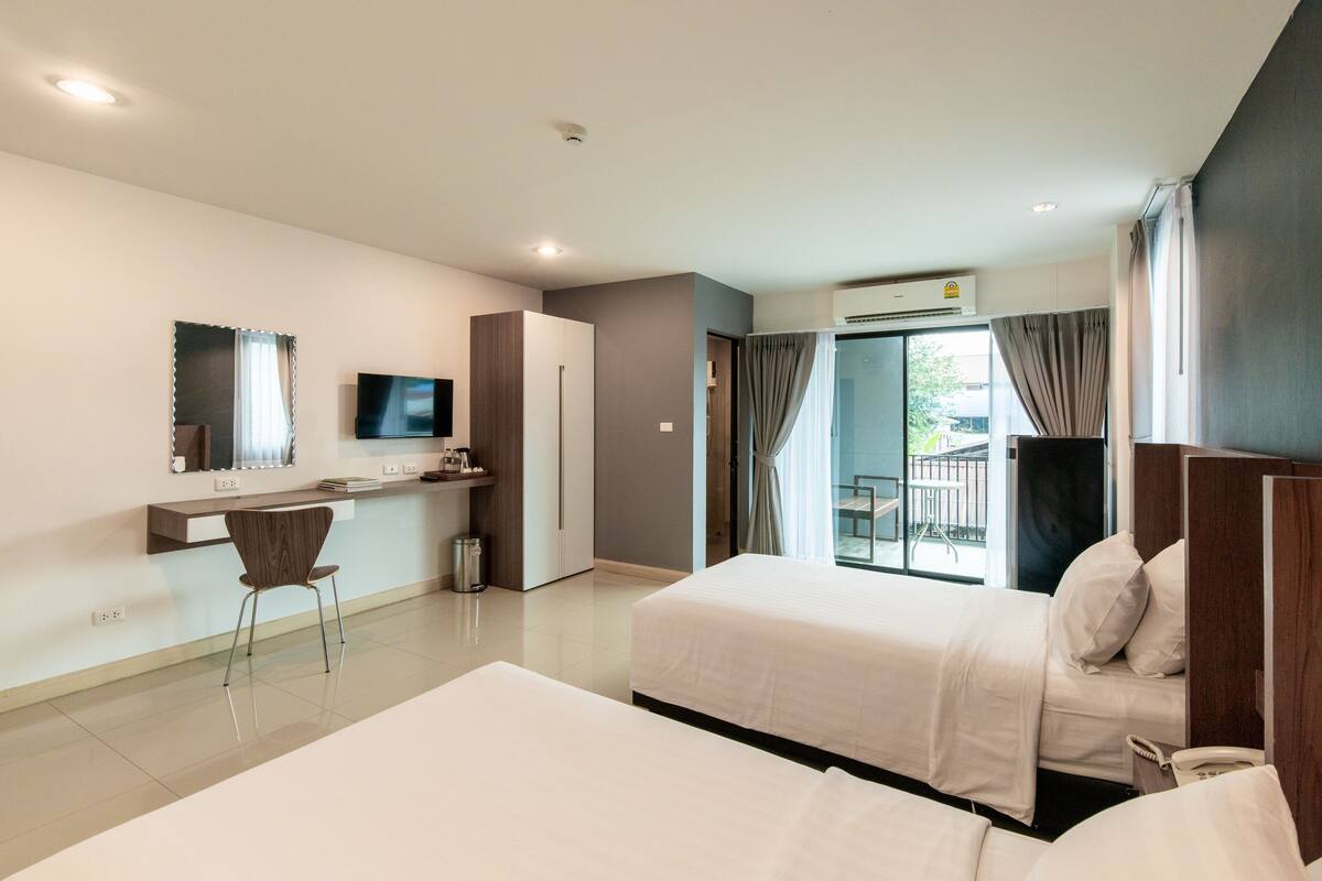 Een moderne hotelkamer met twee bedden, een bureau met stoel, een televisie en een balkon met uitzicht.
