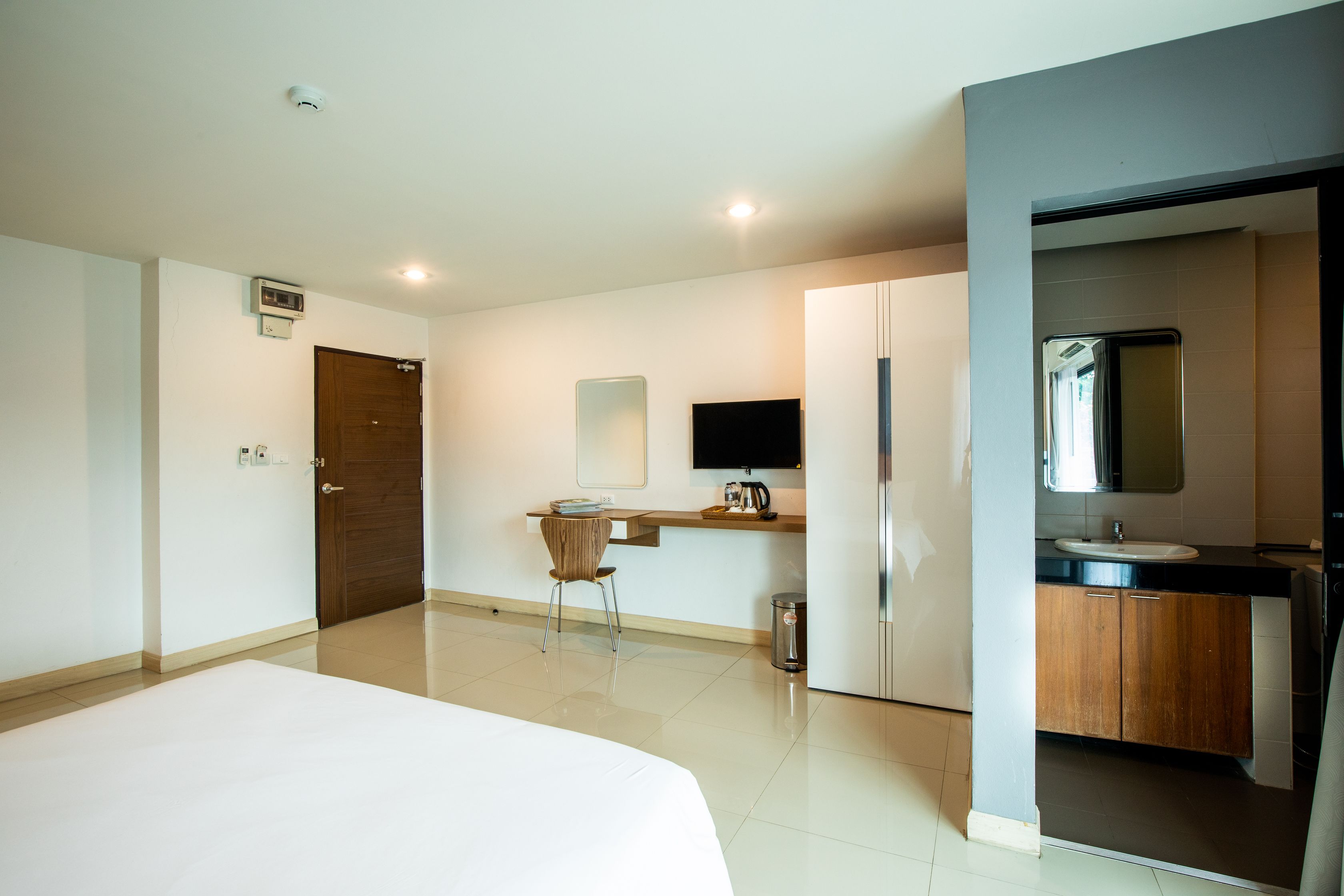 A hotel room with a bed, a desk with a chair, a television, a sink, and a mirror.