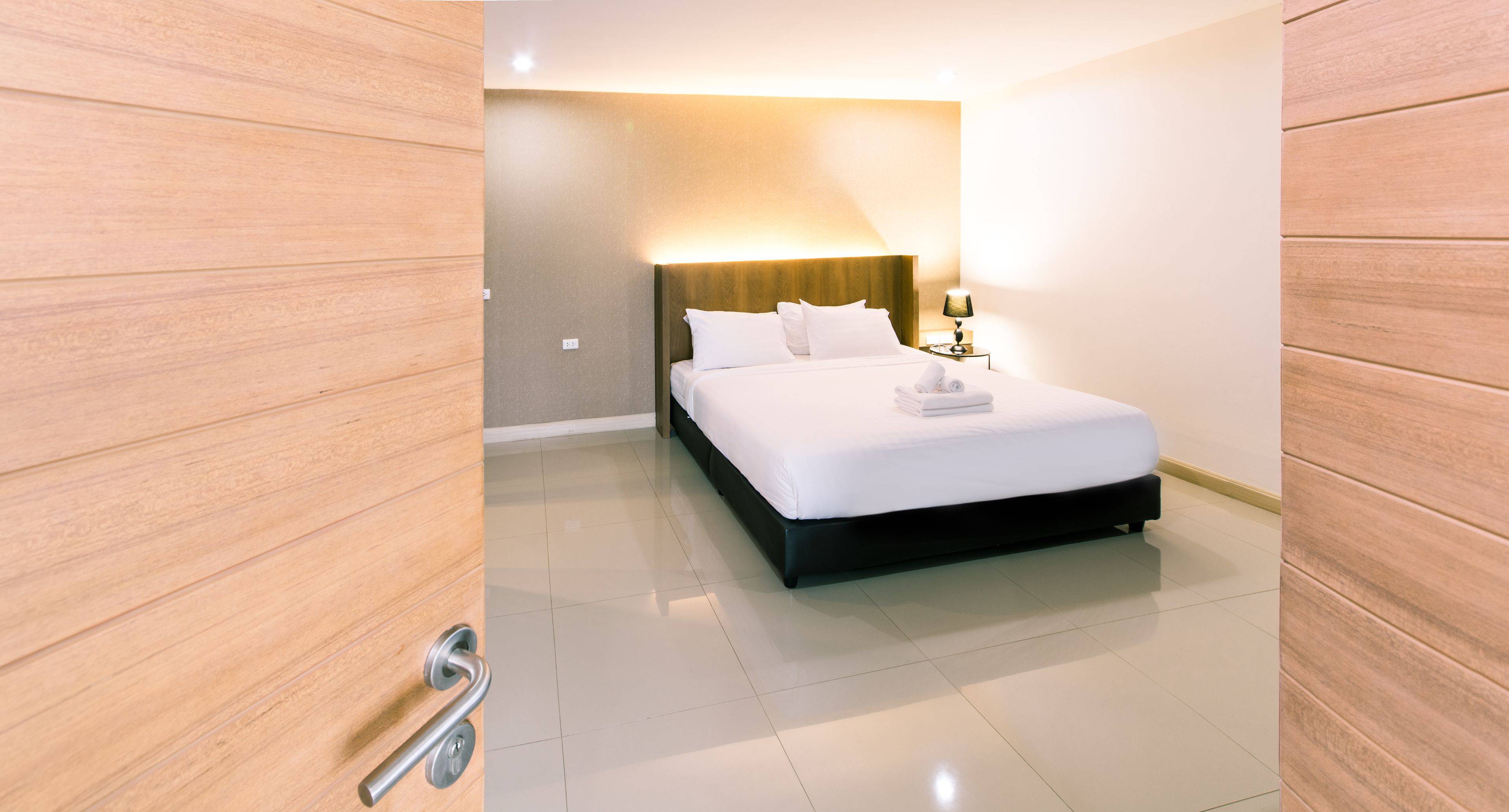 Ein modernes Hotelzimmer mit einem großen Bett, einem Nachttisch mit Lampe und Holzboden.