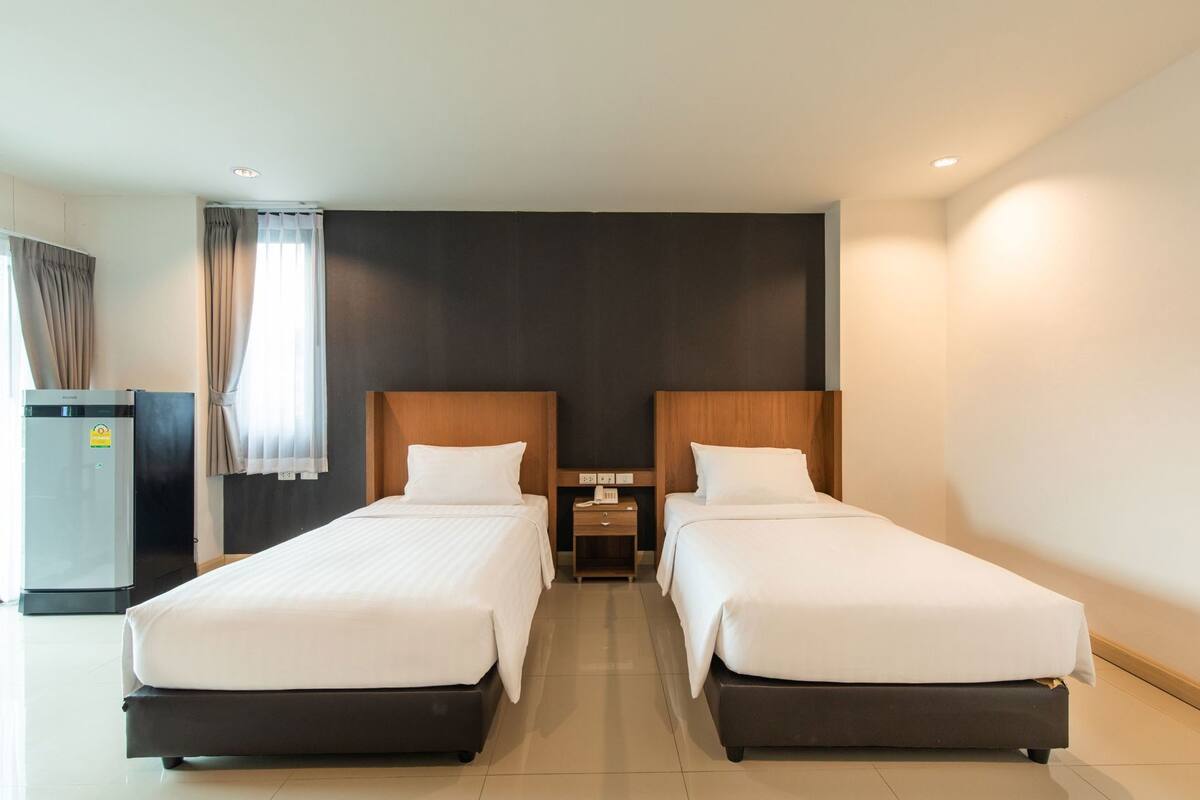 Een hotelkamer met twee bedden, een minibar, een bureau en een raam met gordijnen.