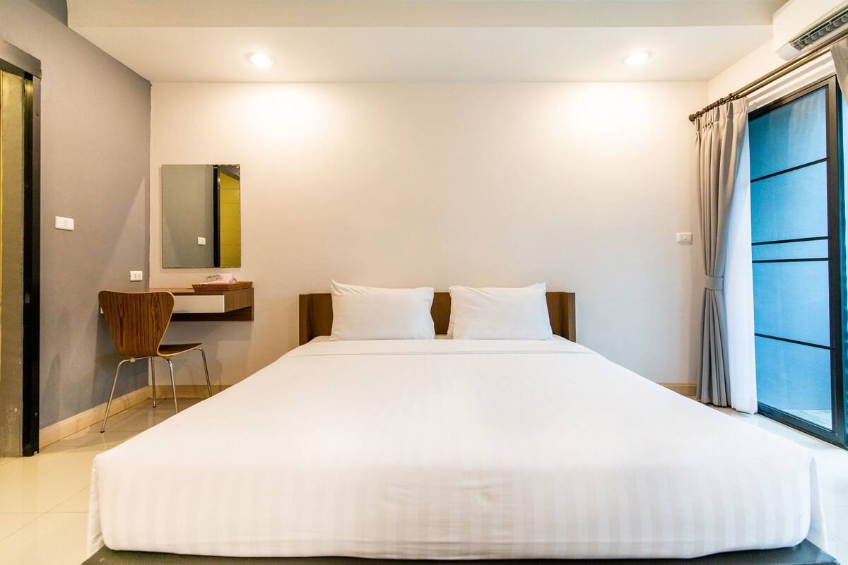 Hotelkamer met een groot bed, een bureau, een stoel, een spiegel en een raam met gordijnen.