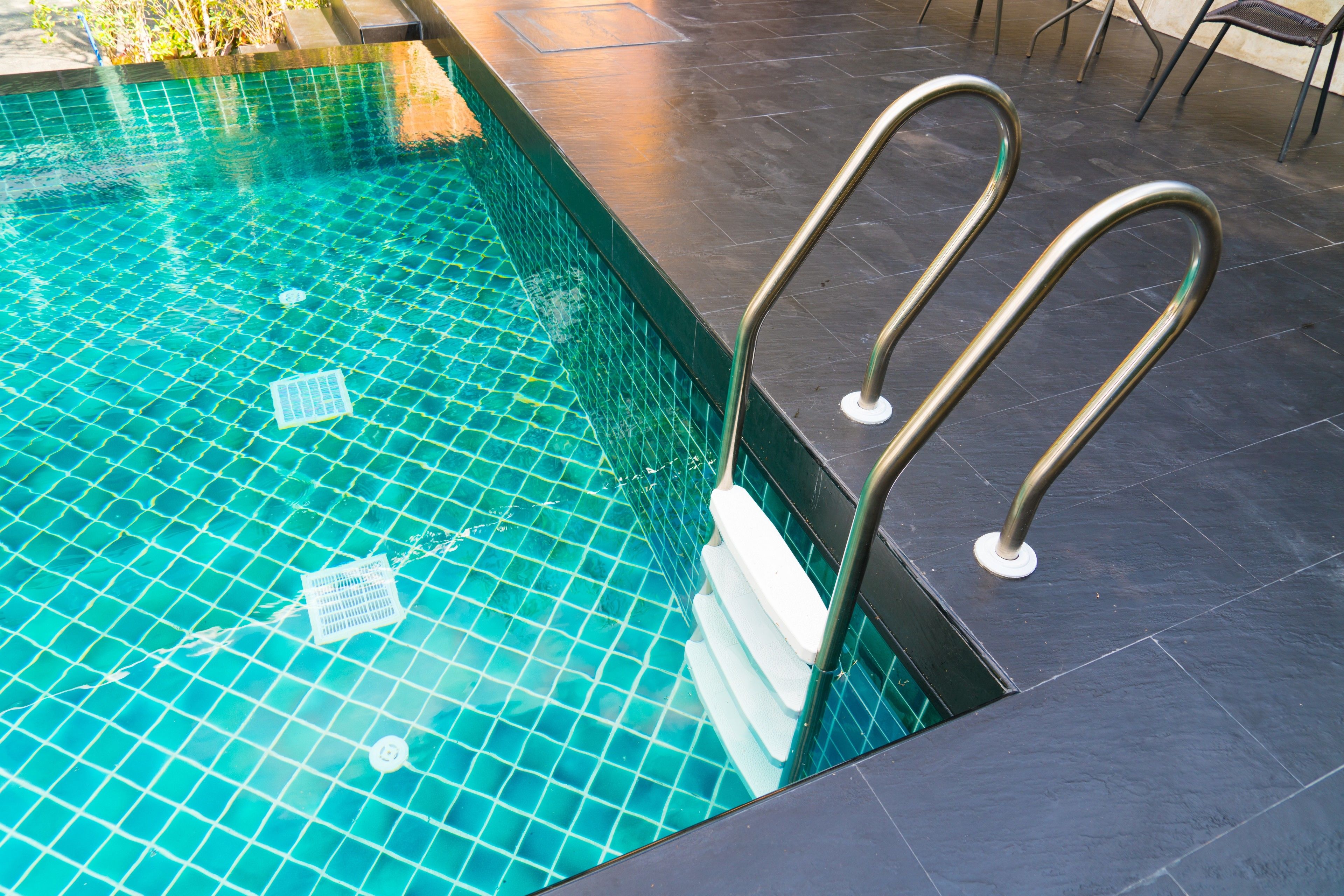 A swimming pool with clear blue water, tiled floor, and metal handrails.