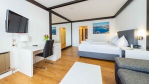 Une chambre d’hôtel moderne équipée d’un lit, d’un bureau et d’une chaise, d’un téléviseur fixé au mur et d’un tableau représentant un paysage.