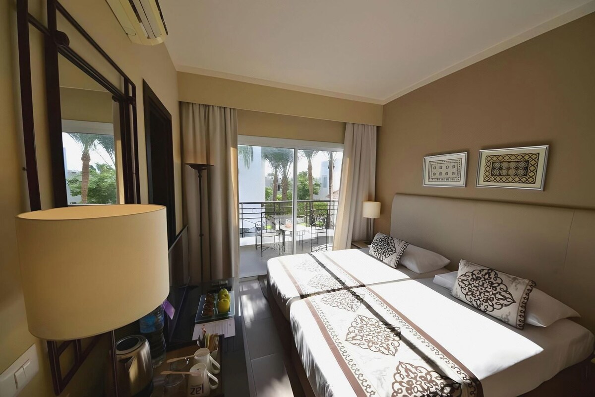 Een hotelkamer met een bed, een bureau, een lamp, een raam en een balkon.