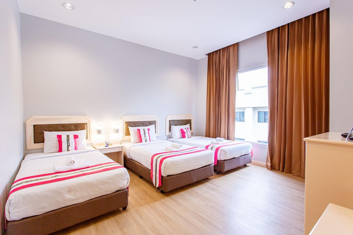 A hotel room with three beds, a desk, and a large window with curtains.