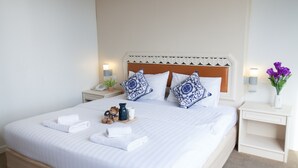 A neatly made bed with white linens, two decorative pillows, a bedside table with a lamp, a phone, a small plant, and a vase with flowers. - The Pawin (Chiang Mai)