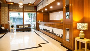A hotel reception area with a reception desk, a sofa, and a clock displaying the time. - The Pawin (Chiang Mai)