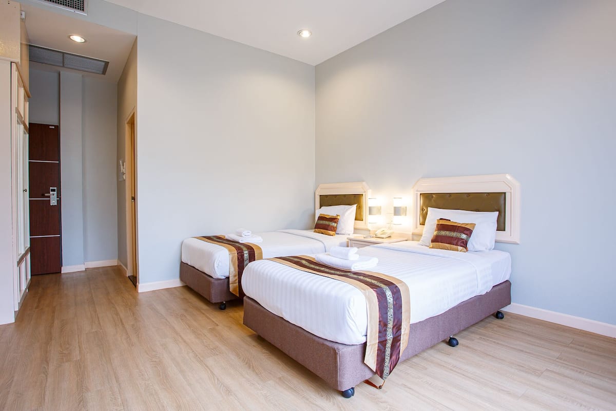 A hotel room with two beds, a wooden floor, a wardrobe, and a bathroom visible through an open door.