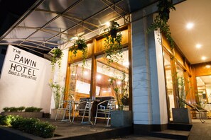 The exterior of The Pawin Hotel with a glass facade, outdoor seating area, and hanging plants. - The Pawin (Chiang Mai)