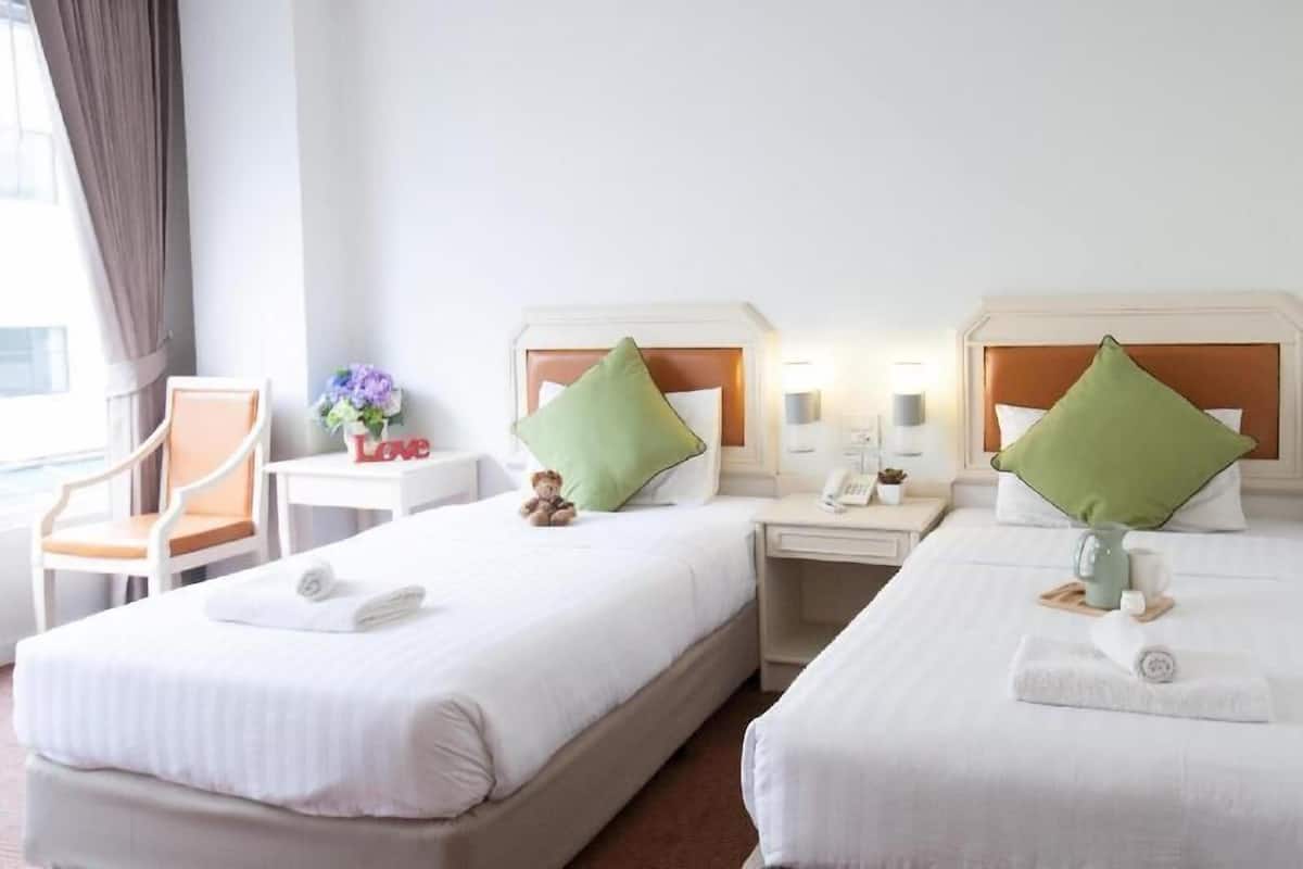 A hotel room with two beds, a chair, a nightstand with a phone, and a small table with a vase and flowers.