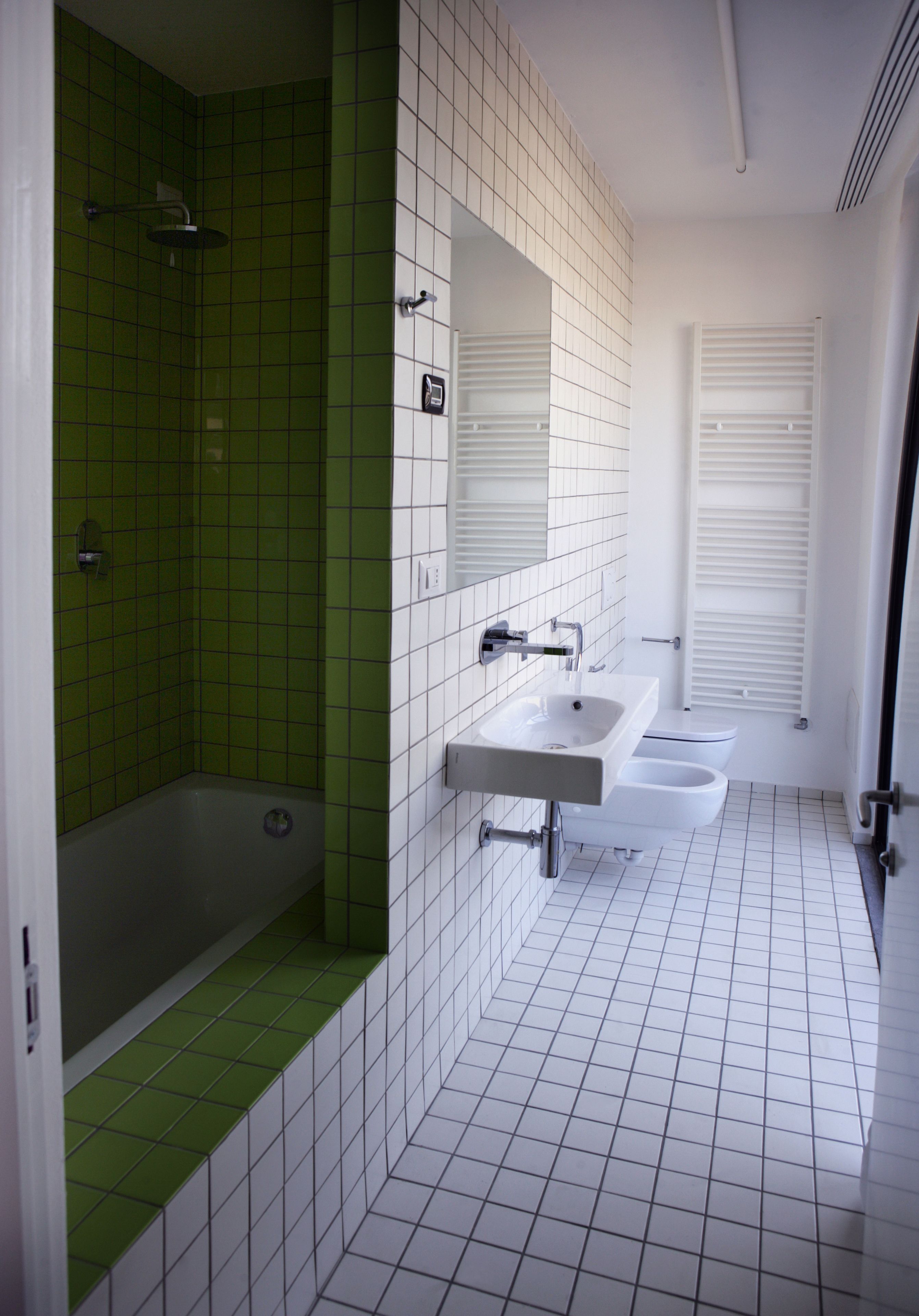 A bathroom with a green-tiled shower, a white sink, and a toilet.