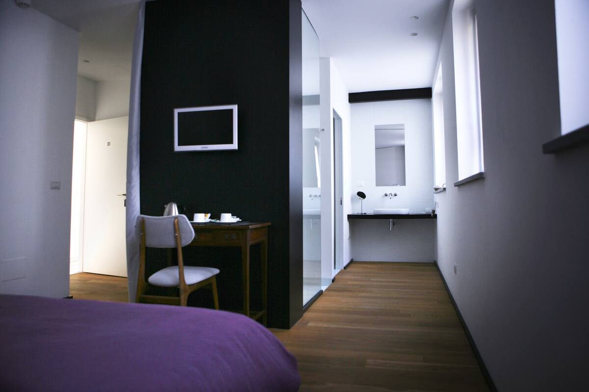 Een slaapkamer met een bed, een bureau en een stoel. Er is een raam en een deur naar een badkamer.