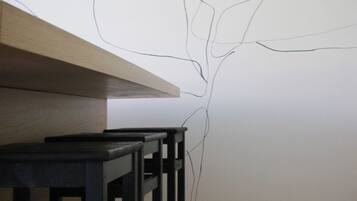 A room with a wooden floor, a white wall with a simple line drawing, and a table with chairs.