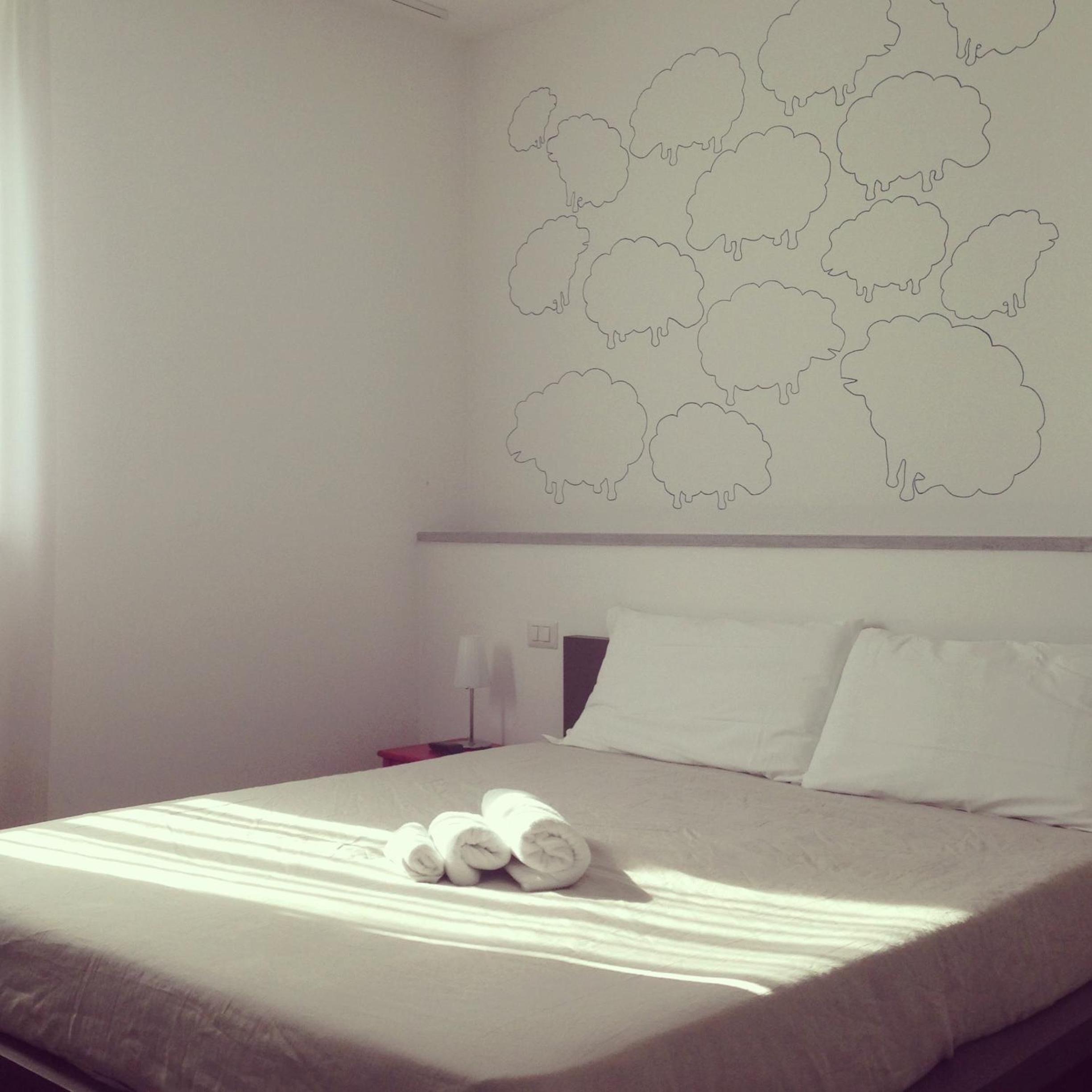 A hotel room with a neatly made bed, a wall with cloud-shaped cutouts, and a bedside table with a lamp.
