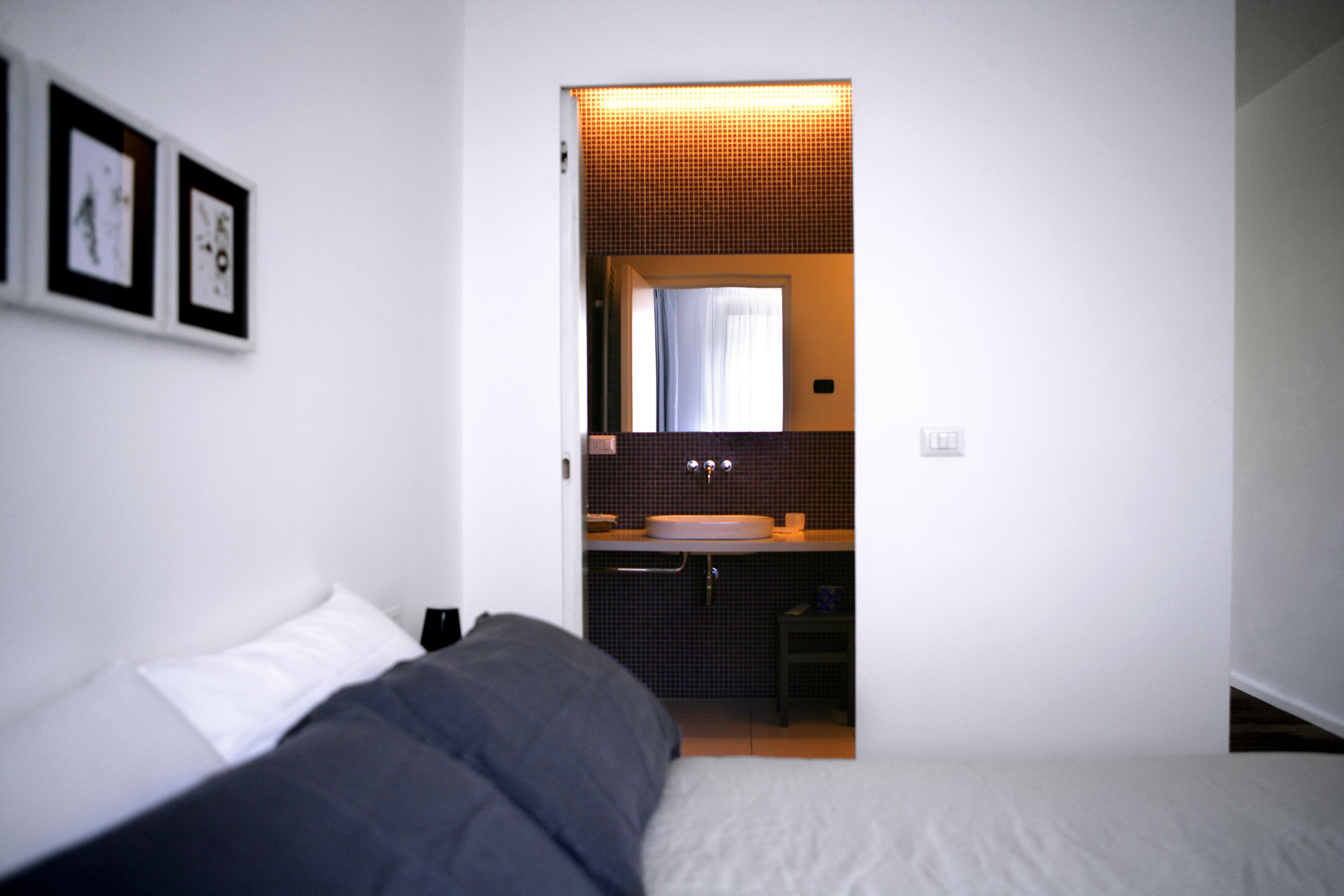 Une chambre avec un lit, une salle de bain avec un lavabo et un miroir, et des tableaux encadrés accrochés au mur.