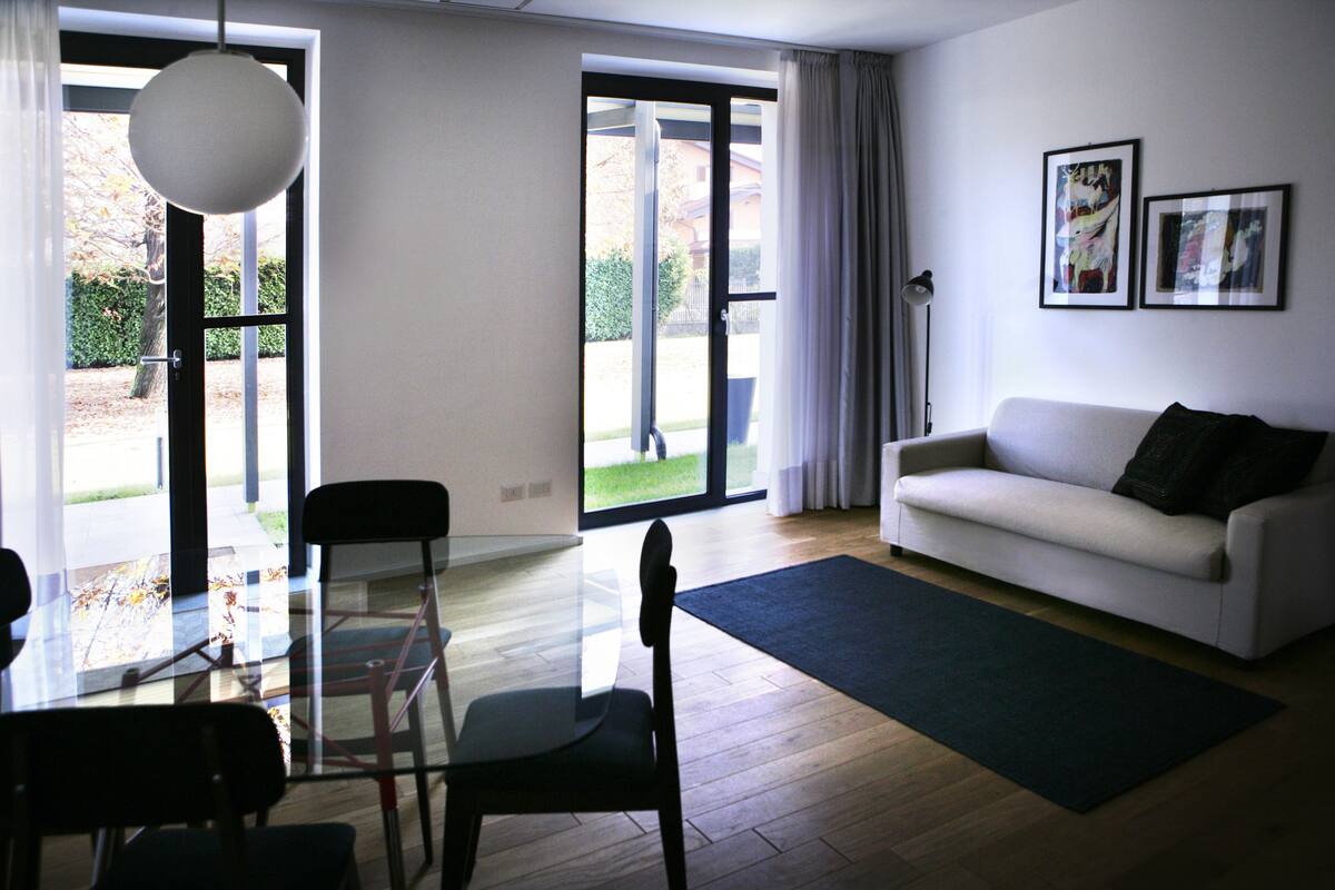 Een moderne woonkamer met een glazen eettafel, een witte bank en twee ingelijste kunstwerken aan de muur.