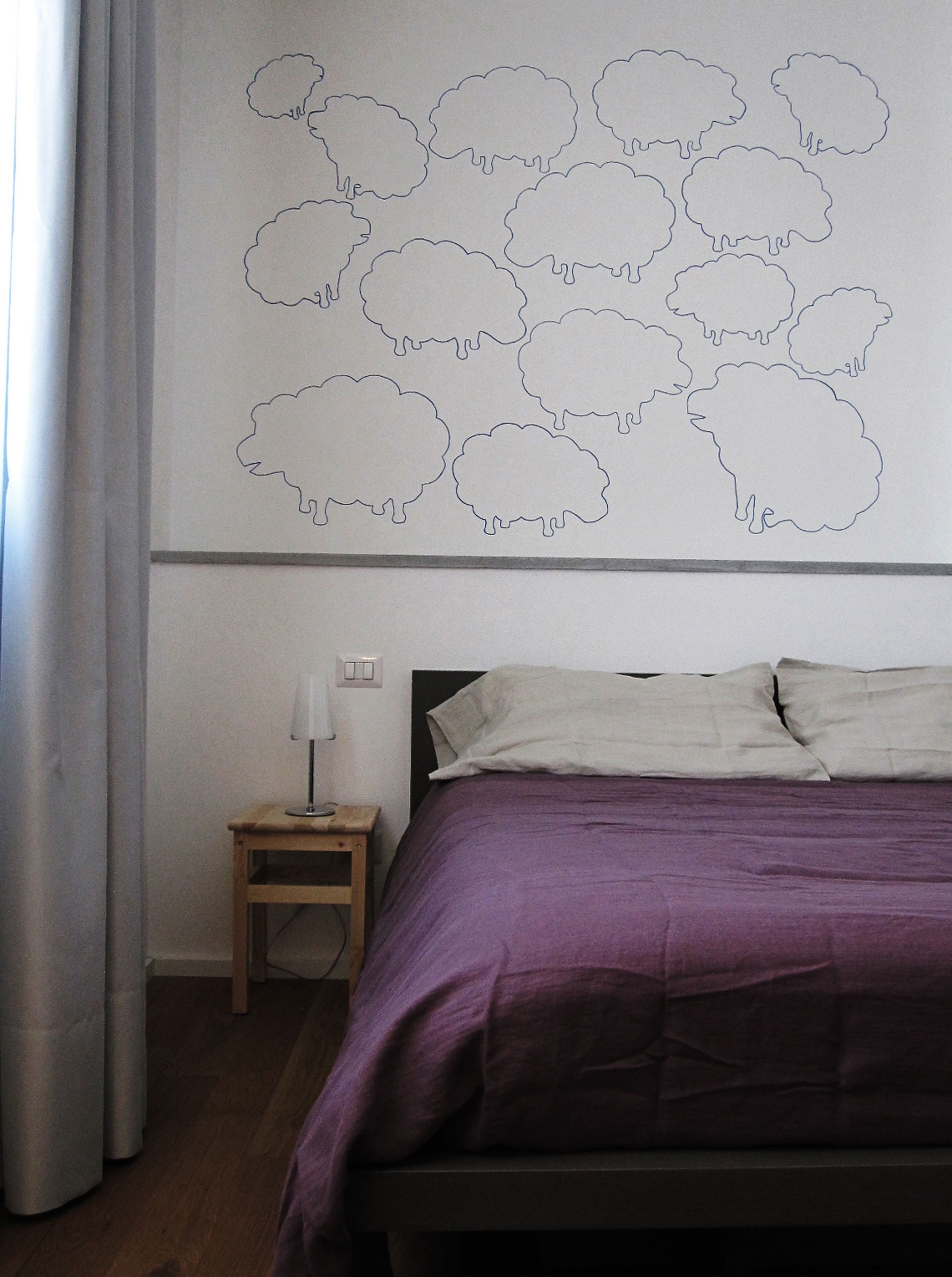A bedroom with a bed, a nightstand, a lamp, and a wall with a sheep outline.