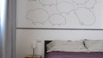 A bedroom with a bed, a nightstand, a lamp, and a wall with a sheep outline.