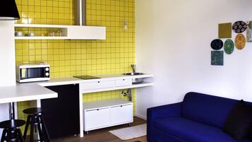 A compact living space with a kitchenette, a blue sofa, and a patterned ottoman.