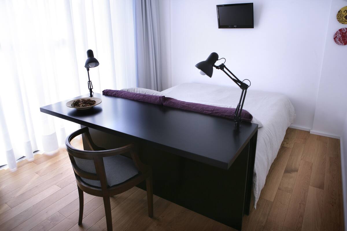 Een slaapkamer met een bed, een bureau, een stoel en een televisie aan de muur.