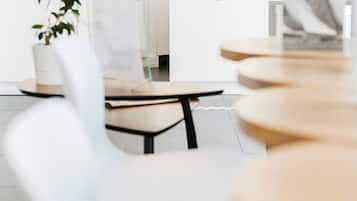 Un hall d'accueil d'hôtel moderne, doté d'un design minimaliste, avec un comptoir d'accueil portant le nom de l'hôtel, « LES VOILES », et son logo. Plusieurs chaises et tables sont disposées pour accueillir les clients, et une plante en pot apporte une touche de verdure.