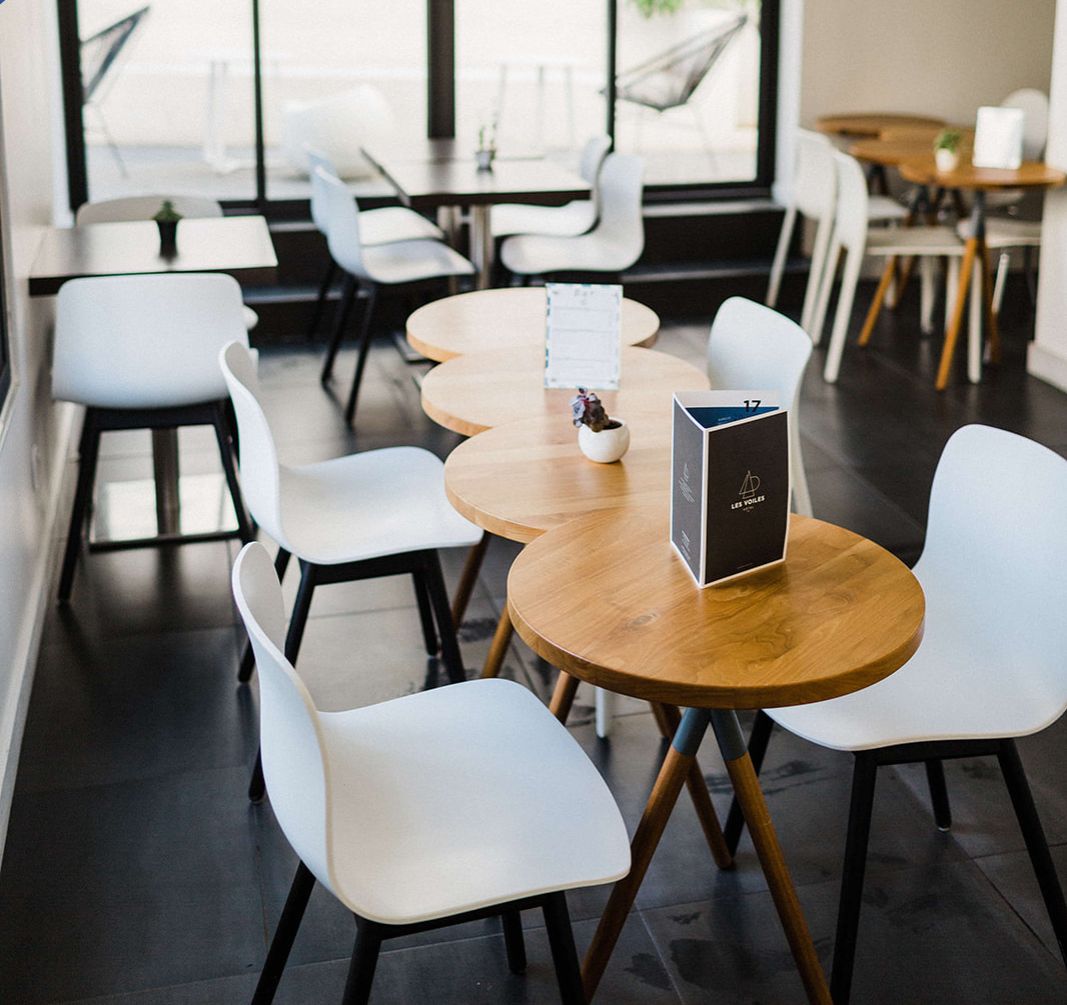 Un'area pranzo moderna con tavoli rotondi e sedie bianche, un espositore per i menu e una vista attraverso ampie finestre.