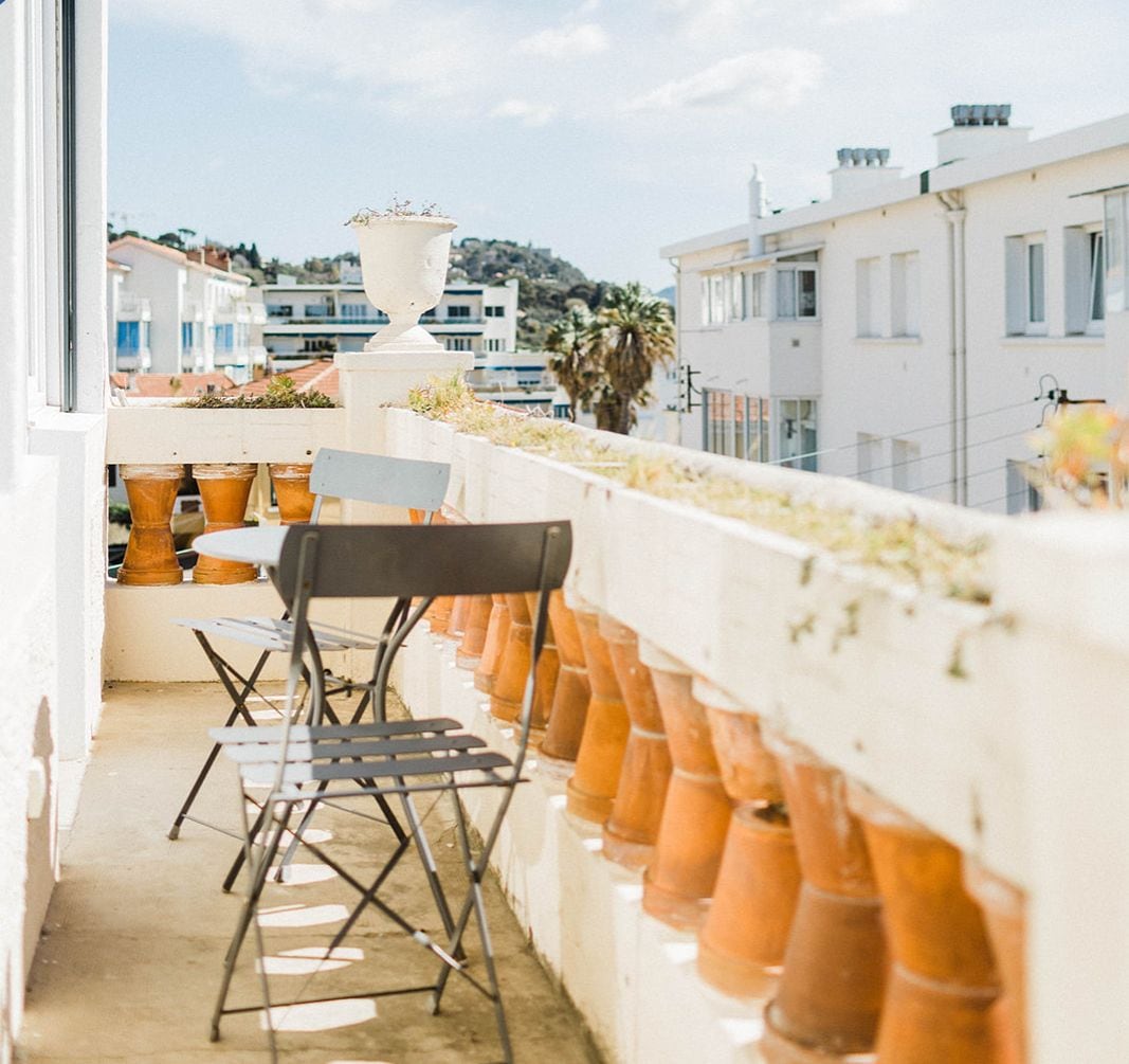 Un balcon orné de pots en terre cuite, une chaise pliante et une vue sur une ville côtière.