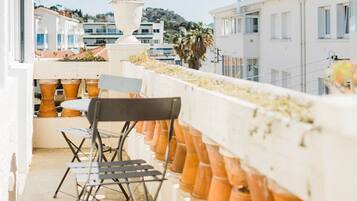 Un balcon orné de pots en terre cuite, une chaise pliante et une vue sur une ville côtière.