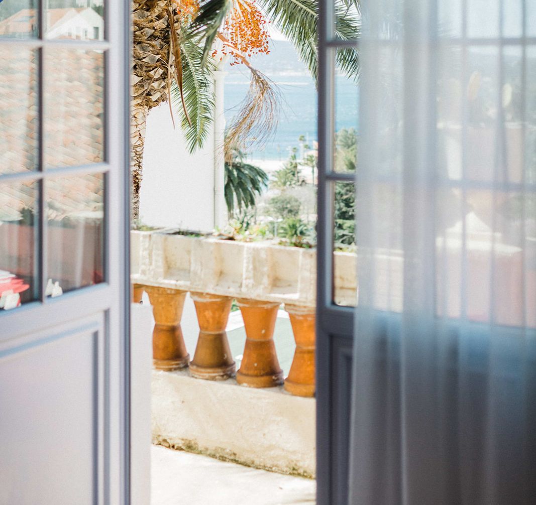 Une vue à travers une fenêtre, avec un palmier tropical et une balustrade en pierre.