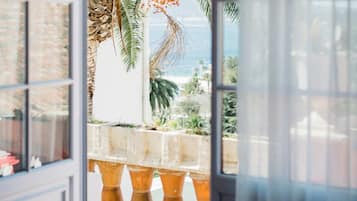 Une vue à travers une fenêtre, avec un palmier tropical et une balustrade en pierre.