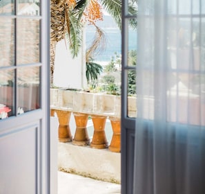 Une vue à travers une fenêtre, avec un palmier tropical et une balustrade en pierre.