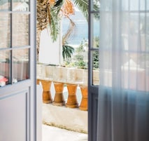 Vista a través de una ventana con una palmera tropical y una barandilla de piedra.