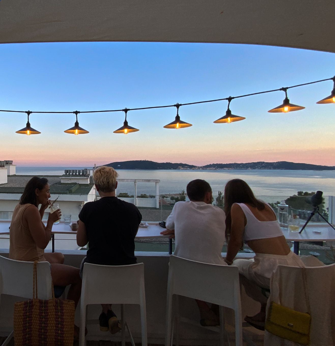 Terraço com vista para o mar, luzes de Natal e pessoas jantando.