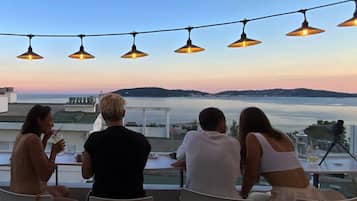Terraço com vista para o mar, luzes de Natal e pessoas jantando.