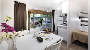 Una habitación compacta con una mesa de comedor preparada para dos personas, una kitchenette, una cama y vistas a una terraza.