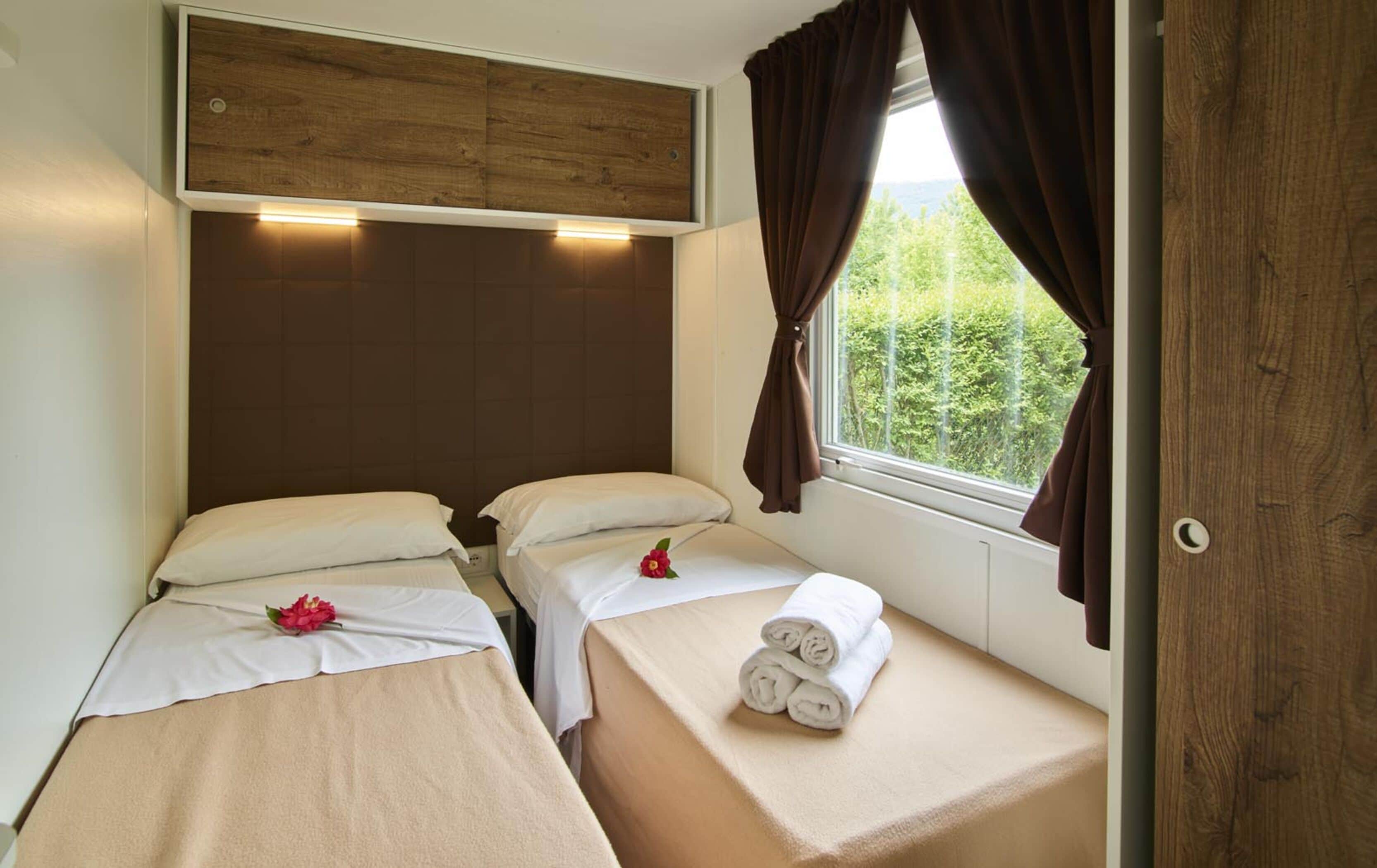 Una habitación pequeña y acogedora con dos camas, un cabecero de madera y una ventana con cortinas.