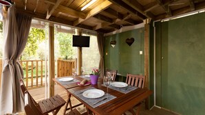 Una terraza de madera con una mesa preparada para dos personas, un televisor montado en la pared y un muro verde decorado con adornos en forma de corazón.
