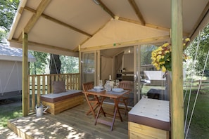 Een houten terras met een tafel, banken, een overdekte zithoek en uitzicht op het interieur.
