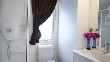 Ein Badezimmer mit Toilette, Dusche und Waschbecken mit Spiegel. Auf dem Waschbecken stehen zwei Vasen mit Blumen.