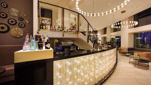 Un bar moderno con una barra curva, varias botellas de licores y una escalera que conduce a un nivel superior.